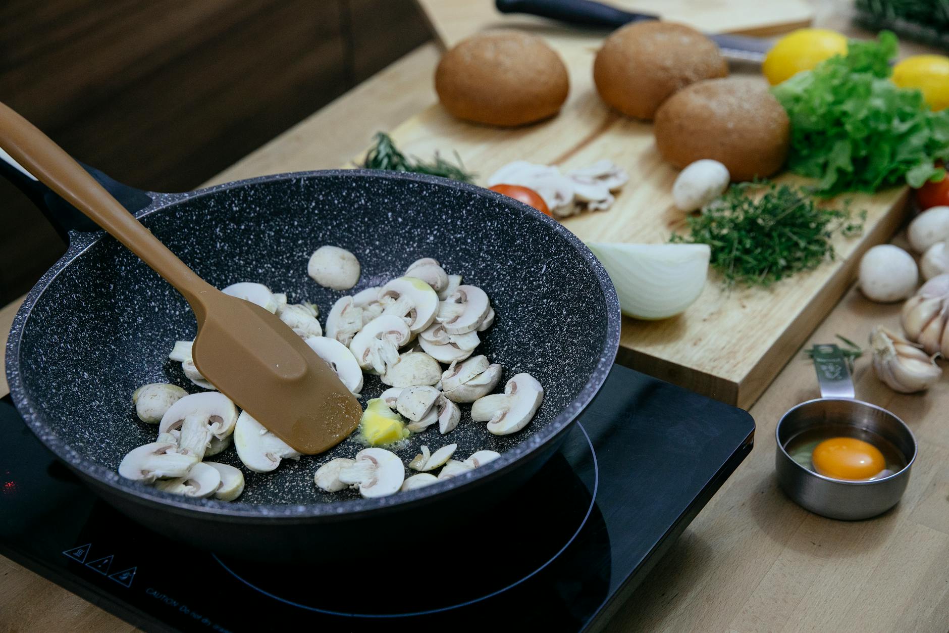 chopped mushrooms in frying pan placed on stove near various veggies and herbs